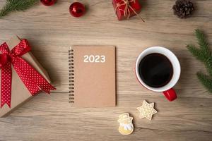 Cuaderno 2023, taza de café negro, galletas navideñas y bolígrafo sobre mesa de madera, vista superior y espacio para copiar. navidad, feliz año nuevo, metas, resolución, lista de tareas, estrategia y concepto de plan foto