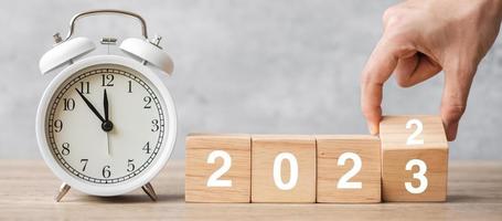 Happy New Year with vintage alarm clock and hand flipping 2022 change to 2023 block. Christmas, New Start, Resolution, countdown, Goals, Plan, Action and Motivation Concept photo