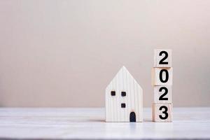 2023 Happy New Year with house model on table wooden background. Banking, real estate, investment, financial, savings and New Year Resolution concepts photo
