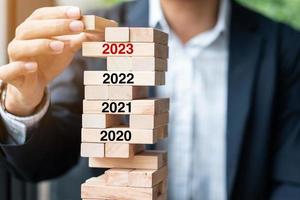 Objetivos para el año 2023, planificación empresarial, gestión de riesgos, conceptos de solución y estrategia. mano de hombre de negocios colocando o tirando de un bloque de madera en la torre