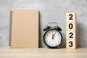 2023 feliz año nuevo con cuaderno en blanco, despertador retro negro y número de madera. concepto de cuenta regresiva, resolución, objetivos, plan, acción y misión foto