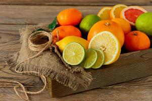 frutas cítricas variadas en una caja de madera. naranja, mandarina, pomelo, limón y lima. sobre un fondo de madera foto