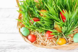 canasta de pascua con hierba verde llena de huevos de pascua de colores brillantes. Felices Pascuas. foto