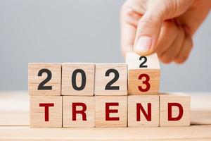 hand flipping block 2022 to 2023 TREND text on table. Resolution, idea, goal, motivation, reboot, business and New Year holiday concepts photo