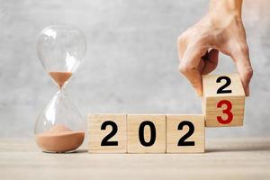 hand flipping block 2022 to 2023 text with hourglass on table. Resolution, time, plan, goal, motivation, reboot, countdown  and New Year holiday concepts photo