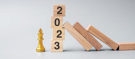 dominó de madera cayendo contra 2023 bloques de parada con figura de rey de ajedrez dorado. negocio, gestión de riesgos, solución, economía, seguros y concepto de año nuevo