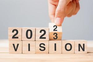 hand flipping block 2022 to 2023 VISION text on table. Resolution, strategy, goal, motivation, reboot, business and New Year holiday concepts photo