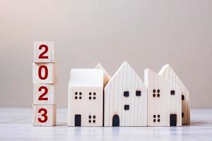 2023 Happy New Year with house model on table wooden background. Banking, real estate, investment, financial, savings and New Year Resolution concepts photo