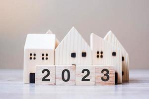 2023 Happy New Year with house model on table wooden background. Banking, real estate, investment, financial, savings and New Year Resolution concepts photo