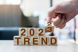 hand flipping block 2022 to 2023 TREND text on table. Resolution, idea, goal, motivation, reboot, business and New Year holiday concepts photo