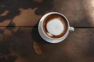 Top view of hot coffee latte cappuccino spiral foam isolated on wood background, photo