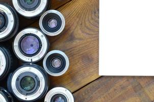 Several photographic lenses and white notebook lie on a brown wooden background. Space for text photo