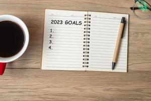 Objetivo 2023 con cuaderno, taza de café negro y bolígrafo sobre mesa de madera, vista superior y espacio para copiar. feliz año nuevo, resolución, lista de tareas, estrategia y concepto de plan foto