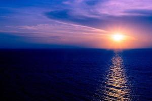 puesta de sol en el mar con nubes y reflejo de agua sobre fondo de colores oscuros. foto