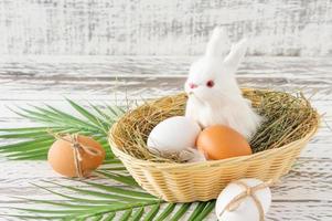 composición festiva de pascua con un pequeño conejito sentado en una canasta con huevo de pascua. concepto de estilo rústico, ecológico y granjero foto
