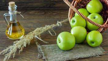 Wicker basket with ripe green apples and bottle of aplle vinegar on wooden background photo