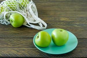 manzanas granny smith orgánicas en un plato con una bolsa textil de malla sobre una mesa de madera. foto