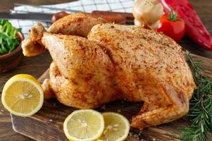 Whole roasted chicken with lemon and vegetbles on cutting board. Wooden rustic background photo