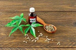 glass bottle with CBD oil, THC tincture and hemp leaves on a wooden table photo