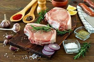 Pieces of raw pork steak with spices and herbs rosemary, salt and pepper on wooden background in rustic style photo