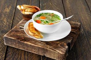 Chicken bouillon with noodles and carrot slices on a wooden table in rustic style photo