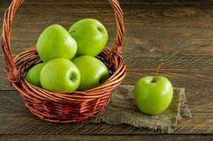 manzanas granny smith orgánicas en una cesta de mimbre sobre una mesa de madera foto