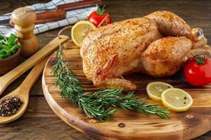 pollo entero a la parrilla con piel caramelizada y romero fresco sobre una mesa de madera. foto