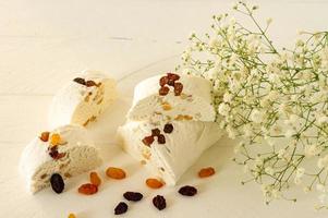 Sliced halva with nuts and dried fruits on a plate served with flowers and fruits on white table photo