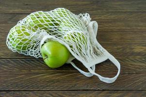 manzanas granny smith orgánicas en una bolsa textil de malla sobre una mesa de madera. foto