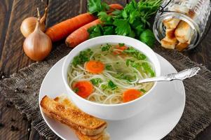 Chicken broth with parsley in a white bowl and croutons on a rustic wooden background. photo