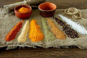 bowls of colourful spices and scattered powder on burlap on wooden background photo