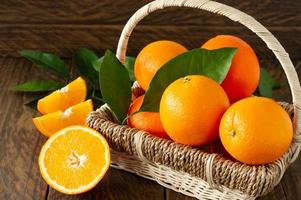 Fresh juicy oranges with green leaves in a basket on wooden background.
