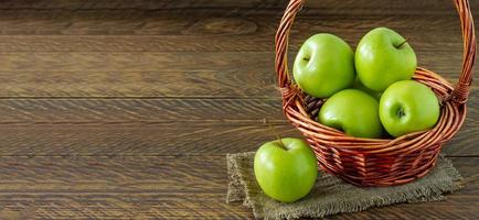 manzanas granny smith orgánicas en una cesta de mimbre sobre una mesa de madera. bandera foto