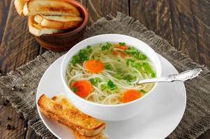 Chicken bouillon with noodles and carrot slices on a wooden table in rustic style photo