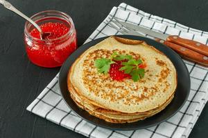 Traditional Russian Crepes Blini stacked in a plate with red caviar on wooden background. Maslenitsa traditional Russian festival meal. Russian food, russian kitchen. Close up.