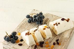 Sliced halva with nuts and dried fruits on a plate served with flowers and fruits on white table photo