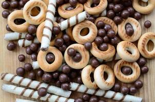 A lot of crispy sweet tubules, chocolate melting balls and yellow bagels lie on a wooden surface. Close up view photo