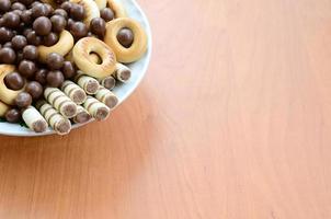 Crispy tubules, chocolate melting balls and bagels lie in a white plate on a wooden table. Mix of various sweets photo