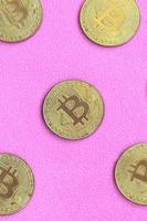 Many golden bitcoins lies on a blanket made of soft and fluffy light pink fleece fabric. Physical visualization of virtual crypto currency photo