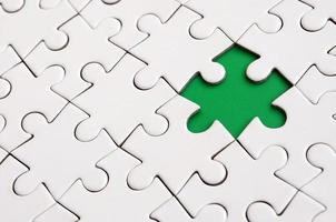 Close-up texture of a white jigsaw puzzle in assembled state with missing elements forming a green pad for text. Copy space photo