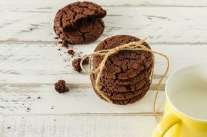 galletas de chocolate para el desayuno con un vaso de leche sobre una mesa de madera blanca. foto