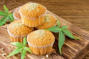 Healthy and tasty vegan and gluten free muffins topped with hemp seeds on a wooden desk close-up. Marijuana cupcake muffins with cannabis leaves photo