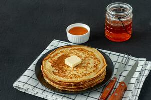 Pancakes served with honey syrup and butter on a dark plate. Traditional crepes for pancake week or Shrovetide. photo