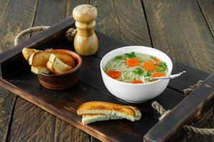 sopa de pollo tradicional con fideos y zanahorias servida en un bol sobre fondo de madera foto