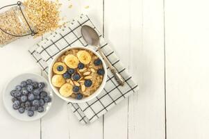 Top view of Bowl of oatmeal wirh blueberry and sliced banana on wooden table. Copy space photo