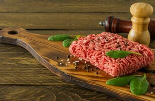 Raw minced beef meat on a wooden cutting board with vegetables and spices. Cooking and healthy eating concept. photo