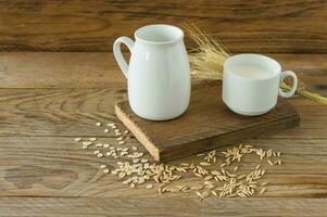 Oat milk in glass pitcher and oatmeal in a cup on a wooden table. photo