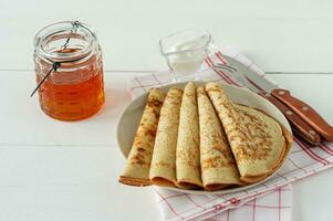 Pancakes with honey syrup on a white plate. Traditional crepes for pancake week or Shrovetide. photo