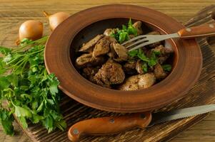 Cooked chicken liver with onion on a plate served on wooden desk. Rustic style photo