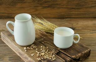 Oat milk in glass pitcher and oatmeal in a cup on a wooden table. photo